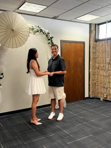 A couple holding hands in a decorated room with plants and hanging decor.